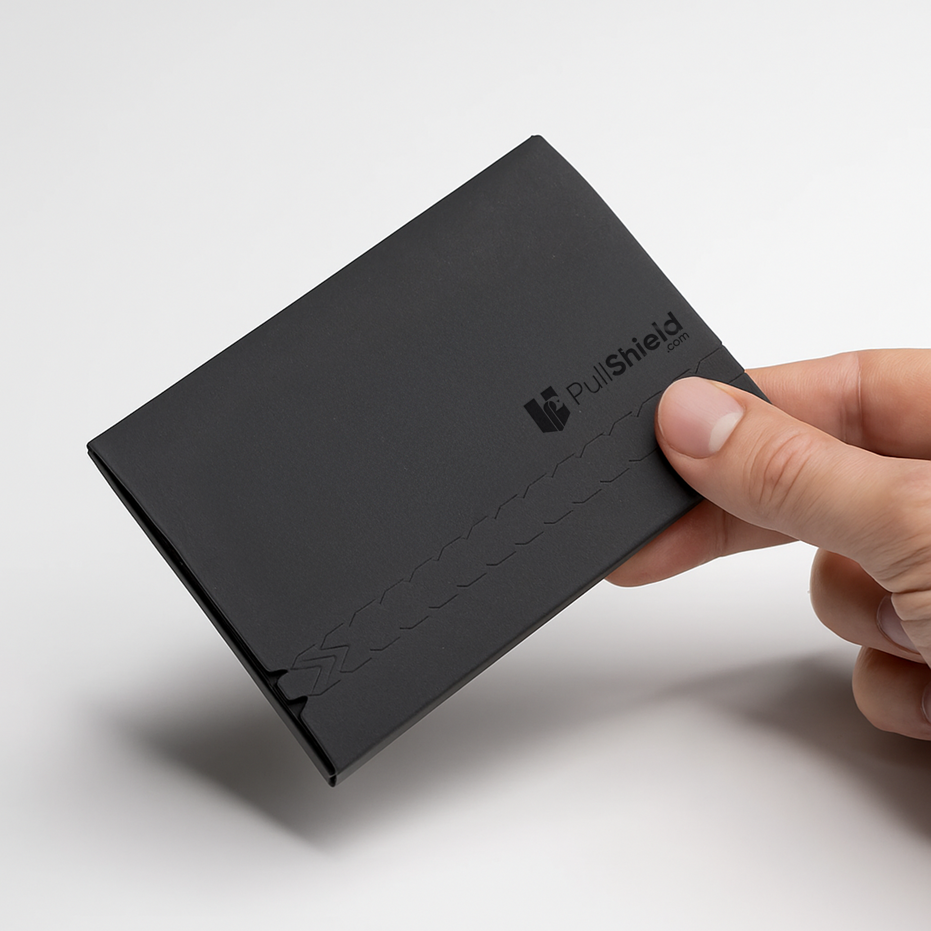 Close-up of a hand holding a sealed black PullShield protective card sleeve with the PullShield logo visible on the front.