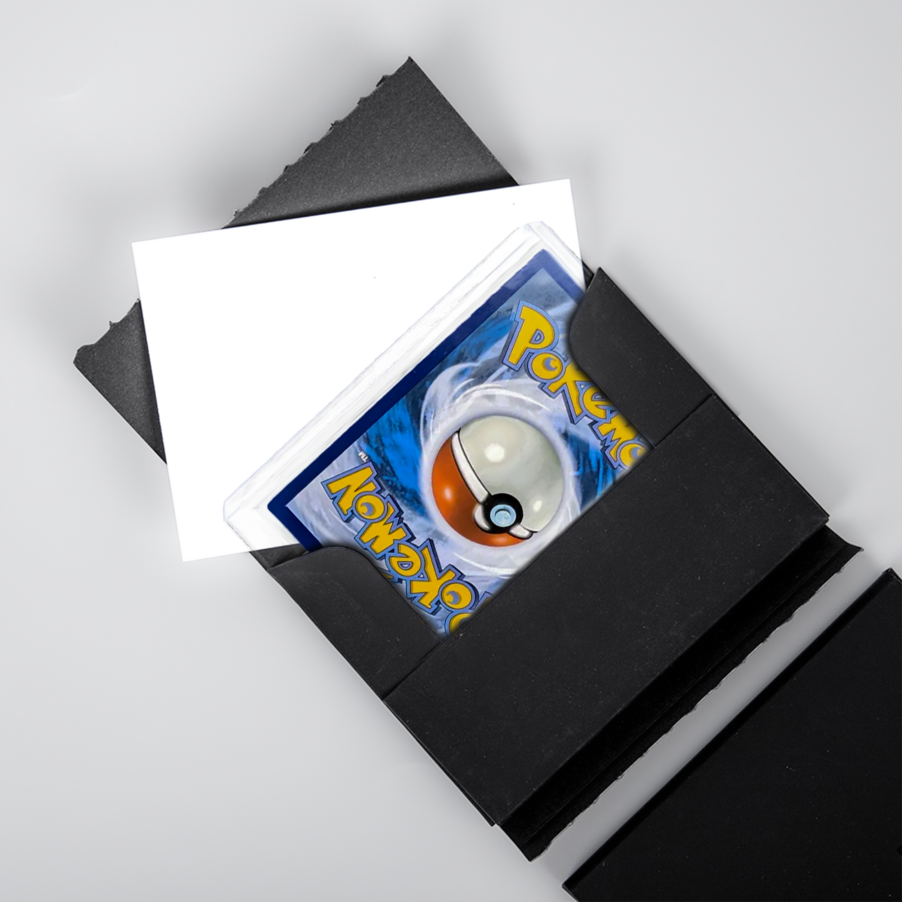 Close-up of a Pokémon card in a top loader being placed inside an open black PullShield protective sleeve, with white cardboard insert visible.